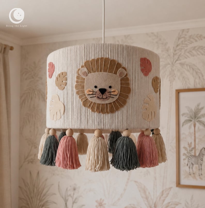 Růžová lampa Safari lev: stínidlo se světlým obličejem, karamelovou hřívou, tvary listů a barevnými střapci.