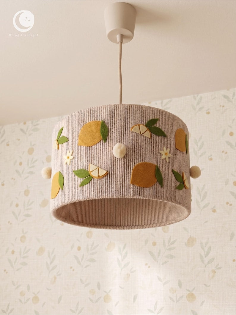 Lampeskærm af neutralt farvet bomuldssnor med filtcitroner, citronskiver, grønne blade, lyse blomster og runde, cremefarvede detaljer.